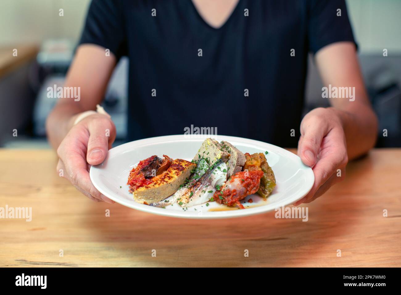 A man standing at a restaurant counter presenting plates of cooked food