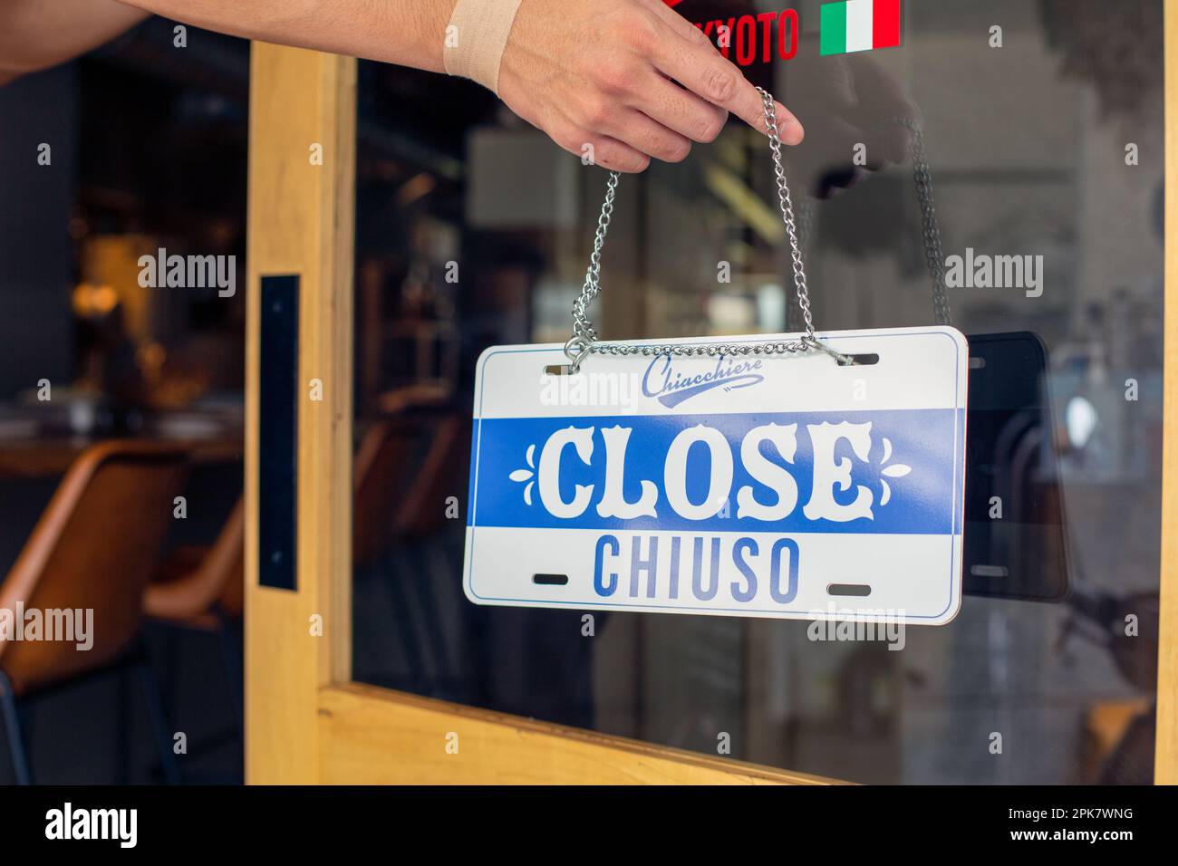 A person hanging up a sign on a restaurant door, reading Close. Closed, dual language, English and Italian. Stock Photo