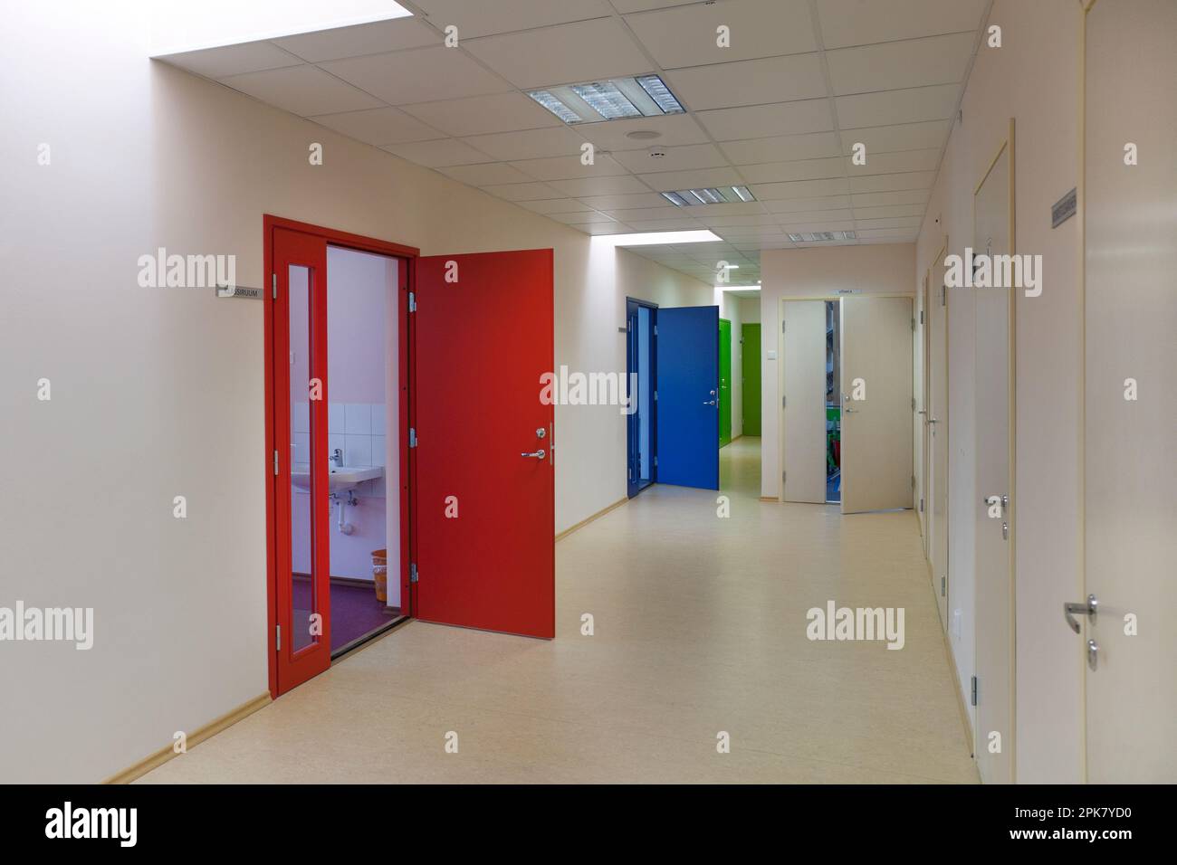 A school corridor with coloured doors opening off it. Red,blue and