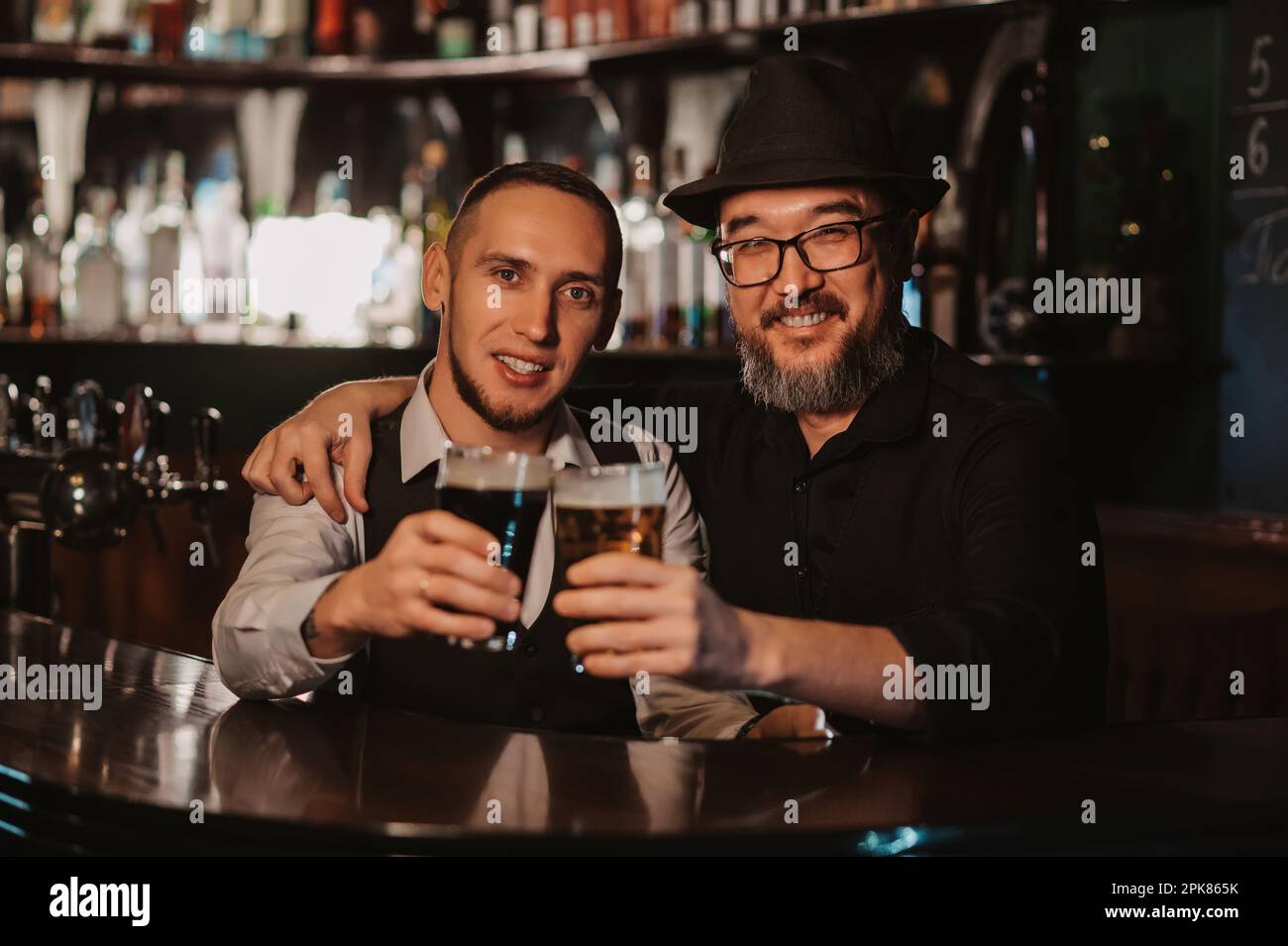 two happy smiling bartenders clink glasses of draft beer at bar counter