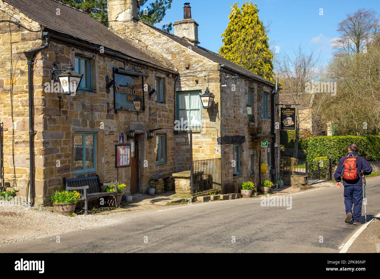 Man  backpacking past the old traditional coaching inn the Cheshire Cheese in the Derbyshire village of Hope at the foot of the great ridge to Mam Tor Stock Photo