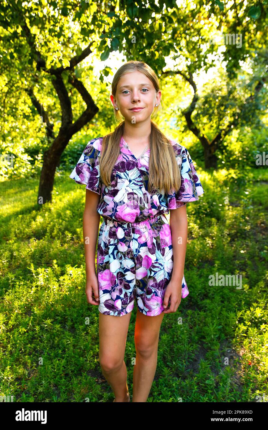 Summer teen girl. Defocus beautiful smiling teenage girl in dress standing against green summer background. High girl 12 or 13 years old on summer law Stock Photo