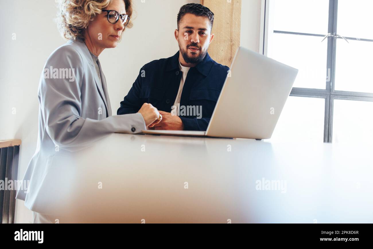 business colleagues looking at a slideshow presentation on a laptop in an office. Two business professionals working on a project together. Stock Photo