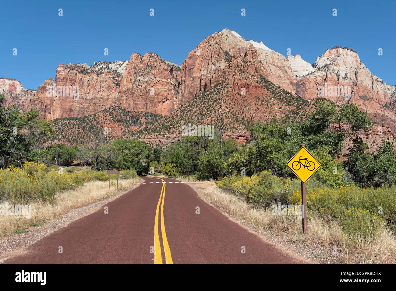 Zion Canyon park road winding through lush vegetation with Cottonwood trees at the foot of steep Navajo Sandstone cliffs towering over the valley Stock Photo