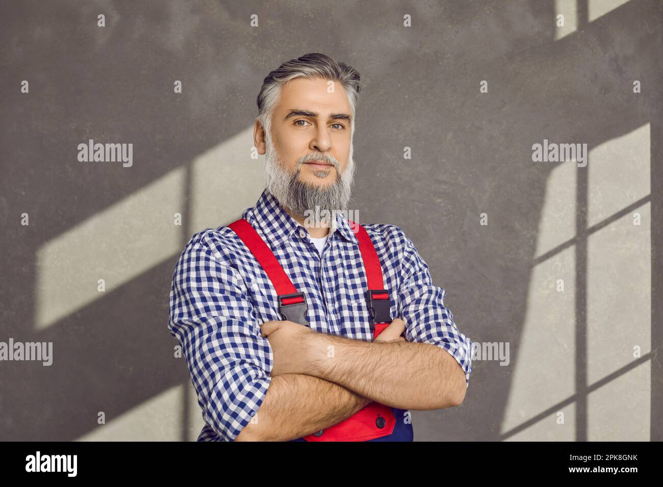 Portrait of a mature repairman in uniform standing on a grey wall background in the house Stock Photo