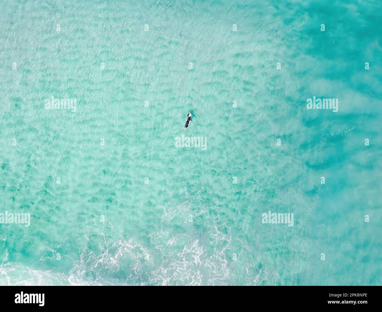 View from above, stunning aerial view of a person surfing on a turquoise ocean. Fuerteventura, Canary Islands, Spain. Stock Photo