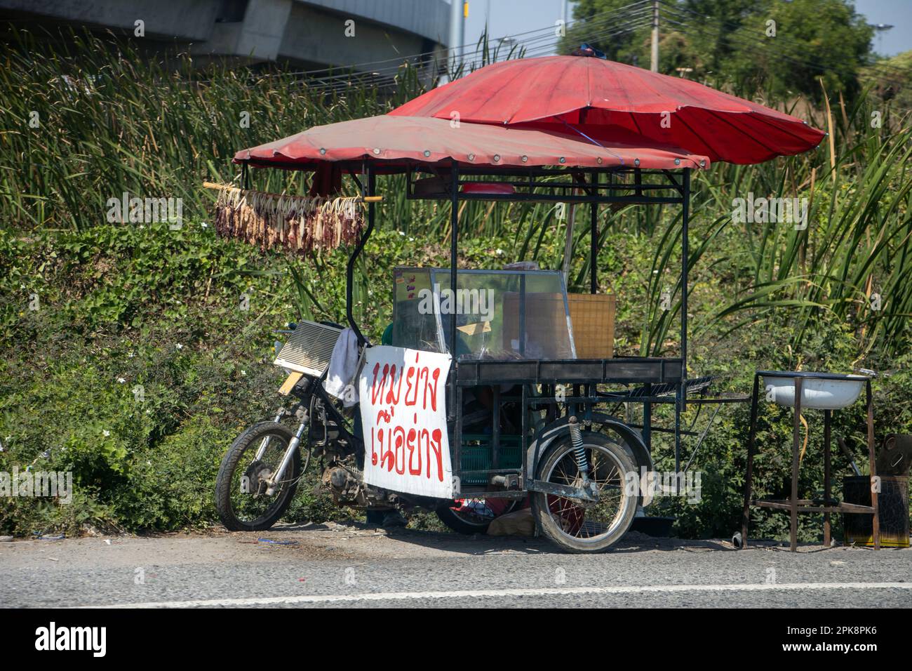 Street kiosk with a billboard offer grilled pork and beef is parked beside a main road, Thailand Stock Photo