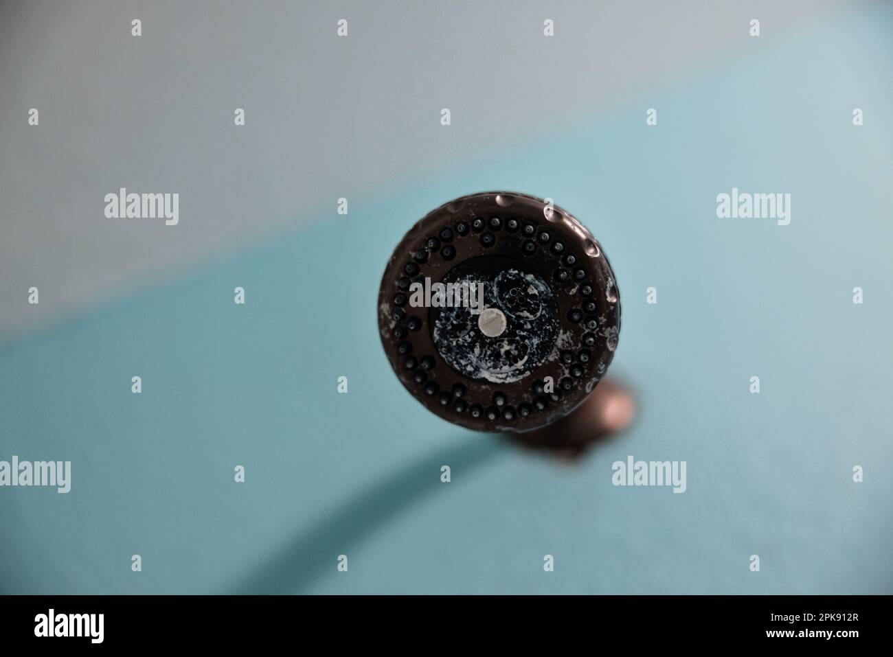 An oil rubbed bronze shower head that needs to be cleaned from a white
