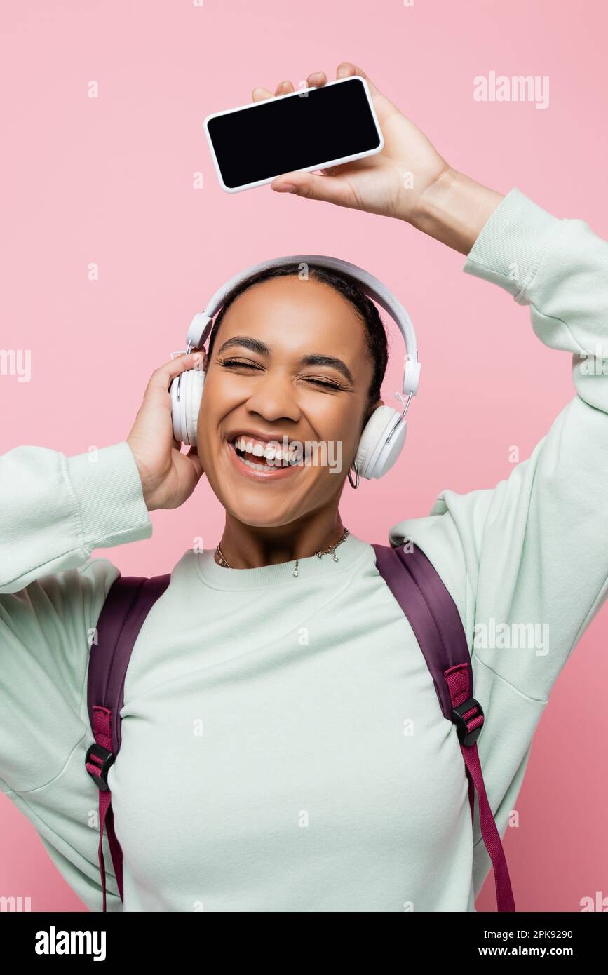 overjoyed african american woman in wireless headphones holding smartphone while listening music isolated on pink,stock image Stock Photo