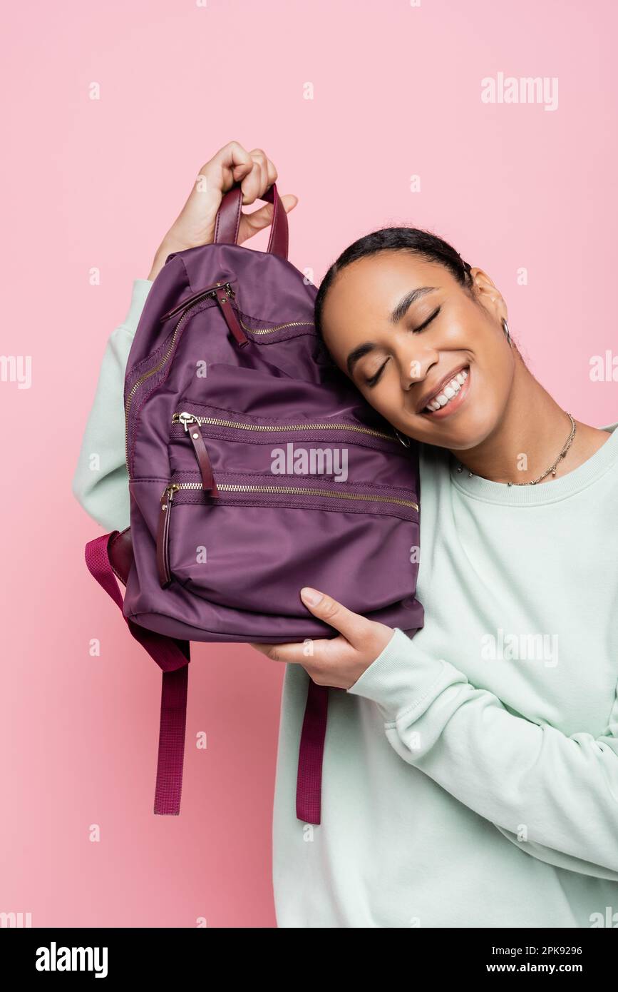 pleased african american student with closed eyes holding purple backpack isolated on pink,stock image Stock Photo