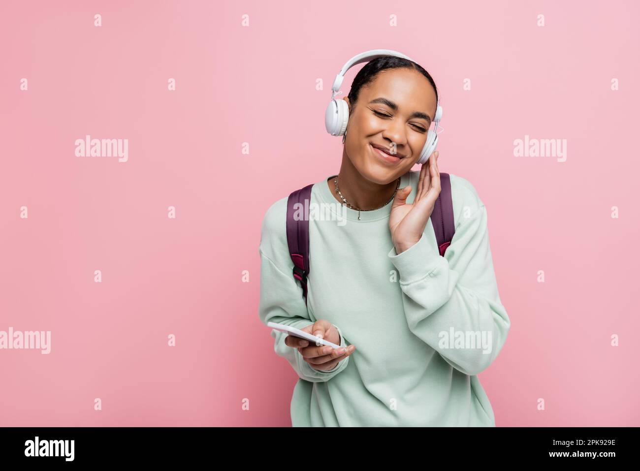 cheerful african american woman in wireless headphones holding smartphone while enjoying music isolated on pink,stock image Stock Photo