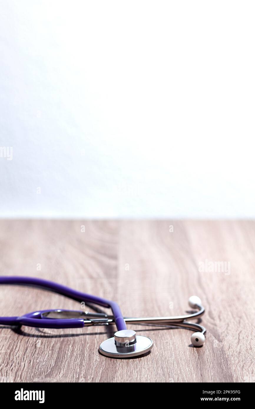 Close-up of the bell and earpiece of a stethoscope over a wooden table. A white wall is on background. Stock Photo