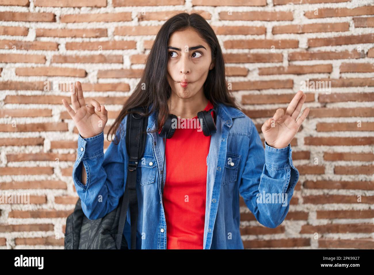 Young teenager girl wearing student backpack doing relax sign making ...