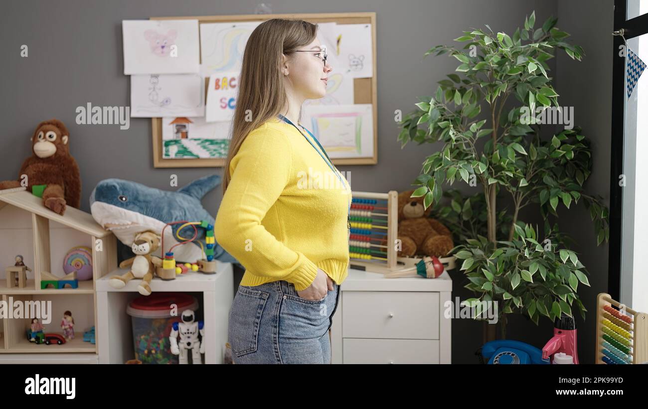 Young blonde woman preschool teacher looking to the side at kindergarten Stock Photo