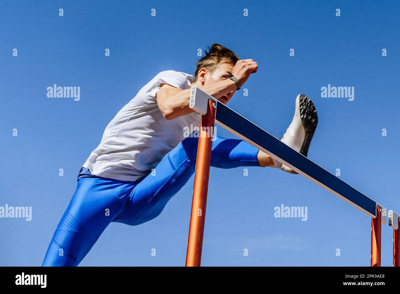 male athlete in blue leggings running attacks hurdles, warm-up in athletics championship Stock Photo