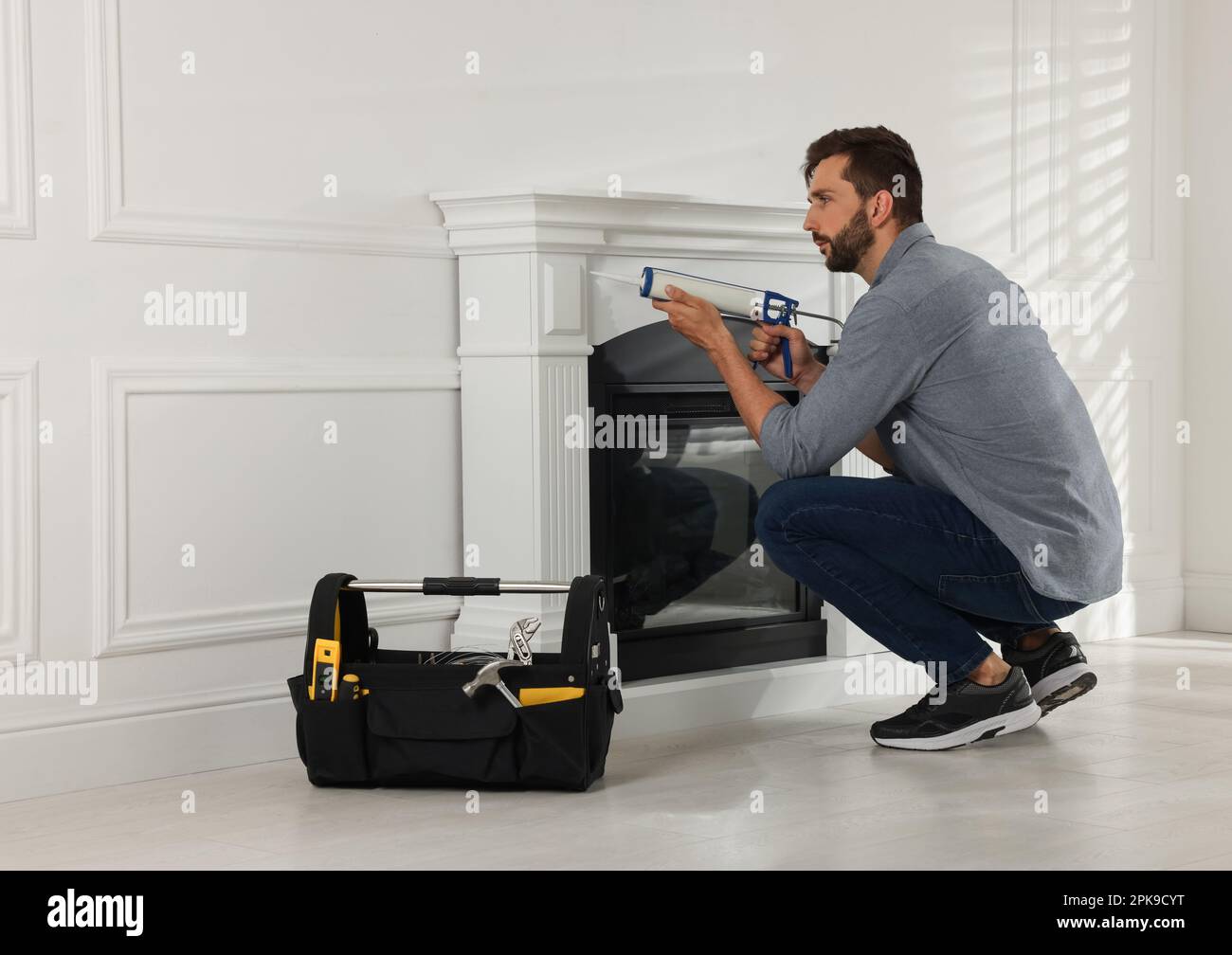 Man sealing electric fireplace with caulk near white wall in room Stock