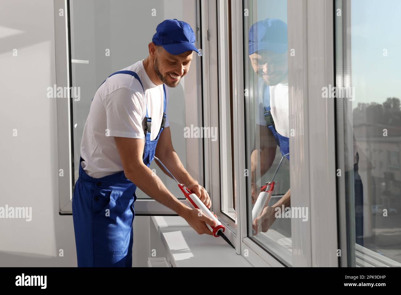 Worker sealing plastic window with caulk indoors. Installation process Stock Photo