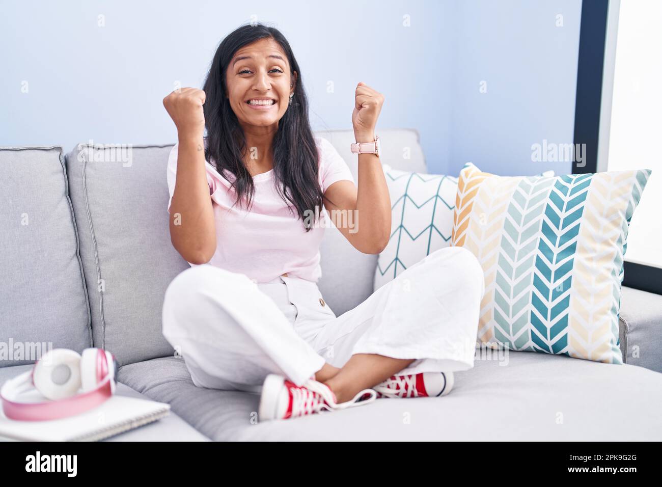 Young hispanic woman sitting on the sofa at home celebrating surprised ...
