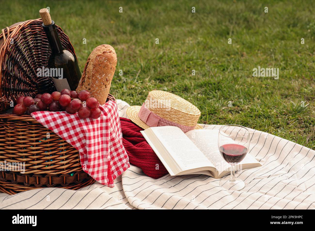https://c8.alamy.com/comp/2PK9HPC/picnic-blanket-with-wicker-basket-wine-food-sweater-straw-hat-glass-and-book-on-green-grass-2PK9HPC.jpg