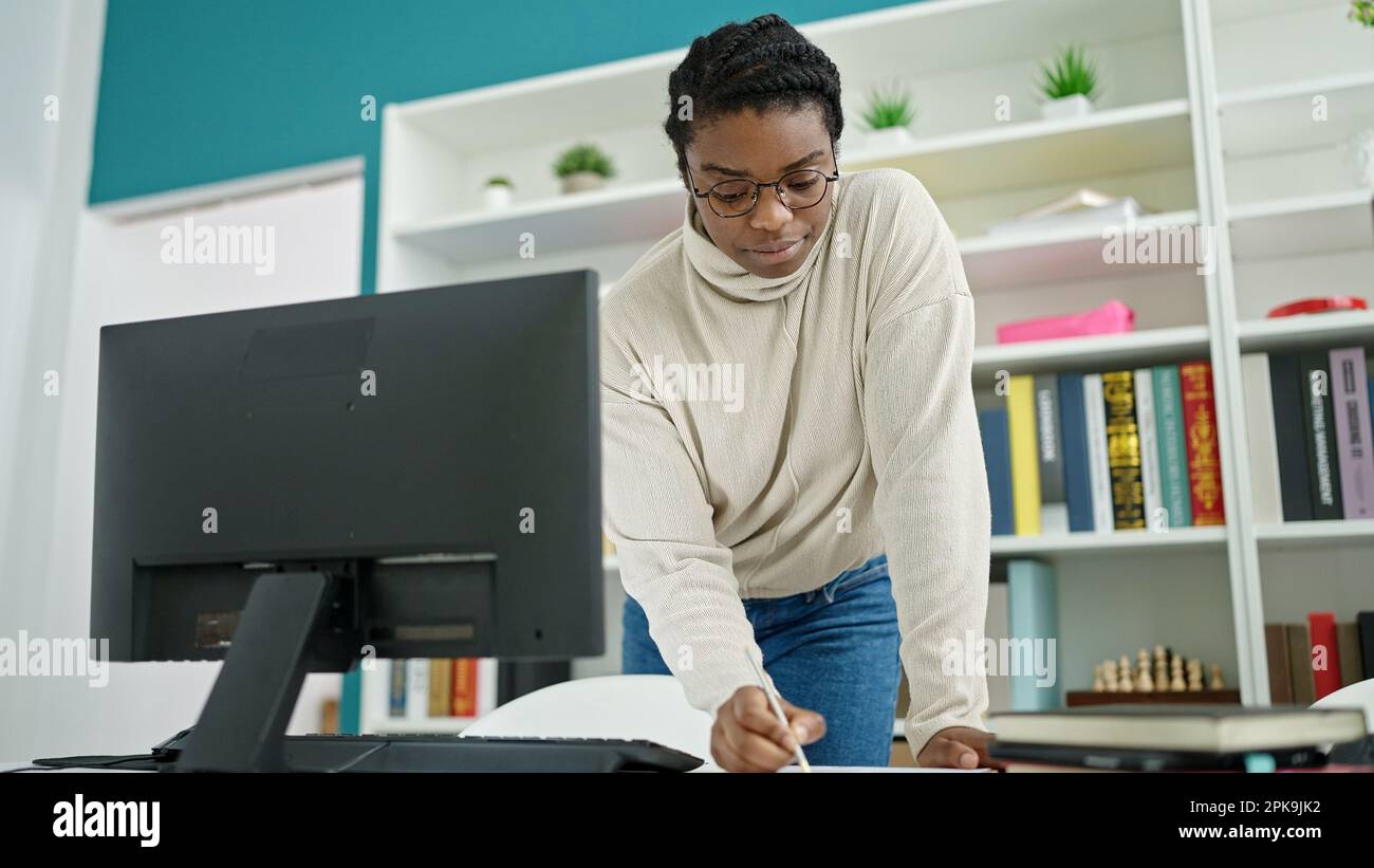 African american woman student using computer writing on notebook at ...