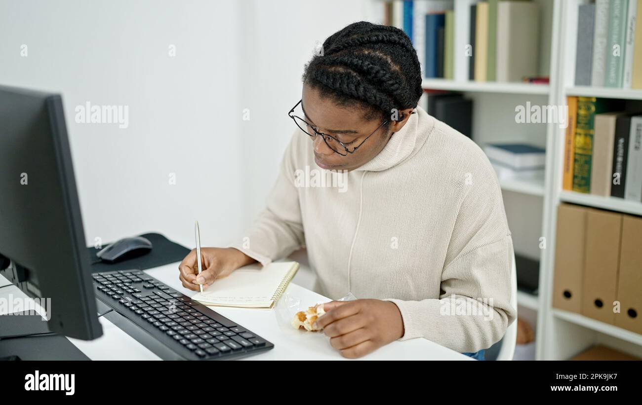 African american woman student writing on notebook eating waffle at ...