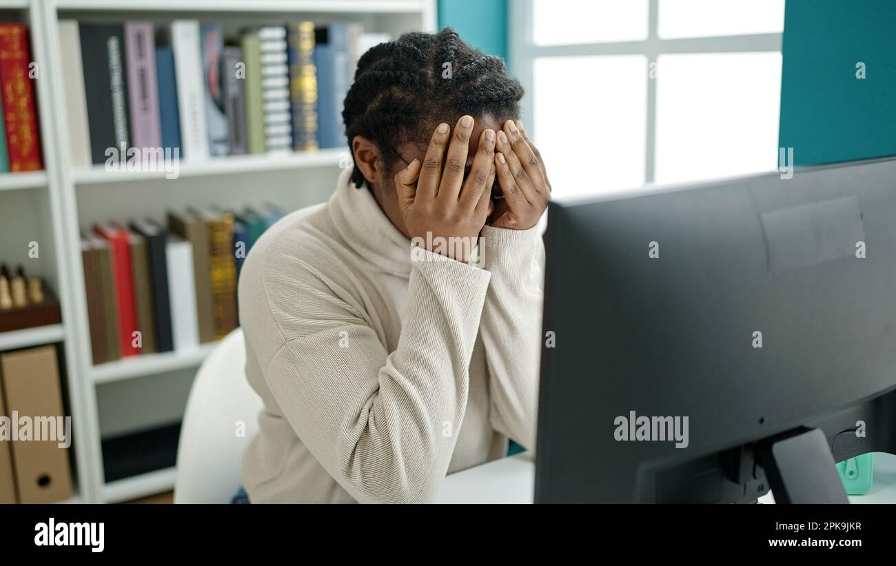 African american woman student using computer stressed at library ...