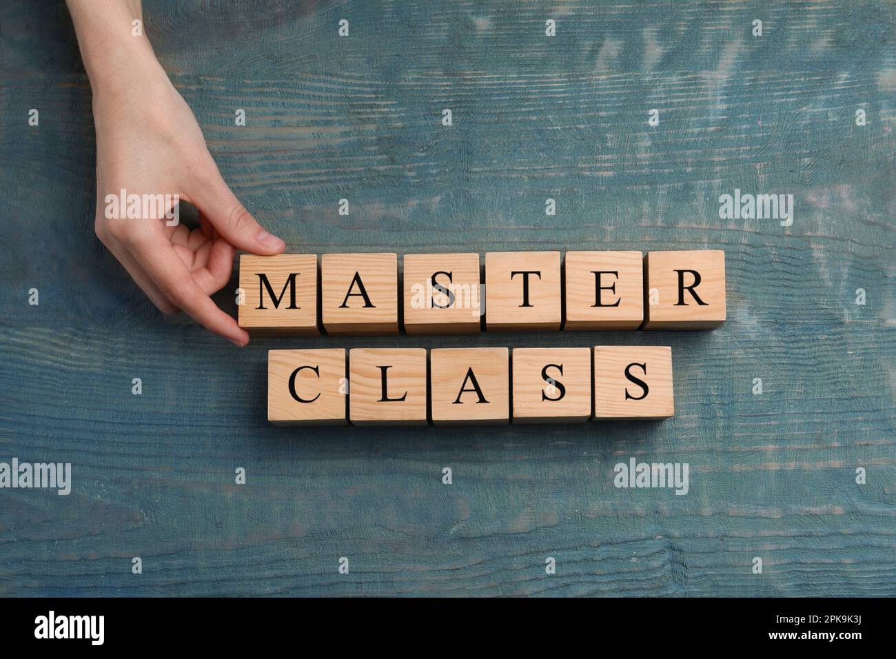 Woman making words Master Class with cubes at light blue wooden table, top view Stock Photo