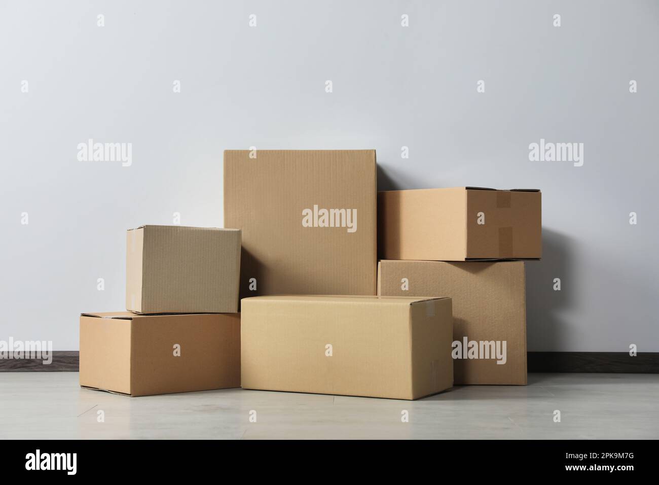 Many closed cardboard boxes on floor near white wall. Delivery service ...
