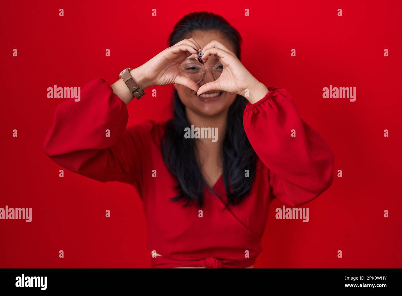 Asian young woman standing over red background doing heart shape with ...