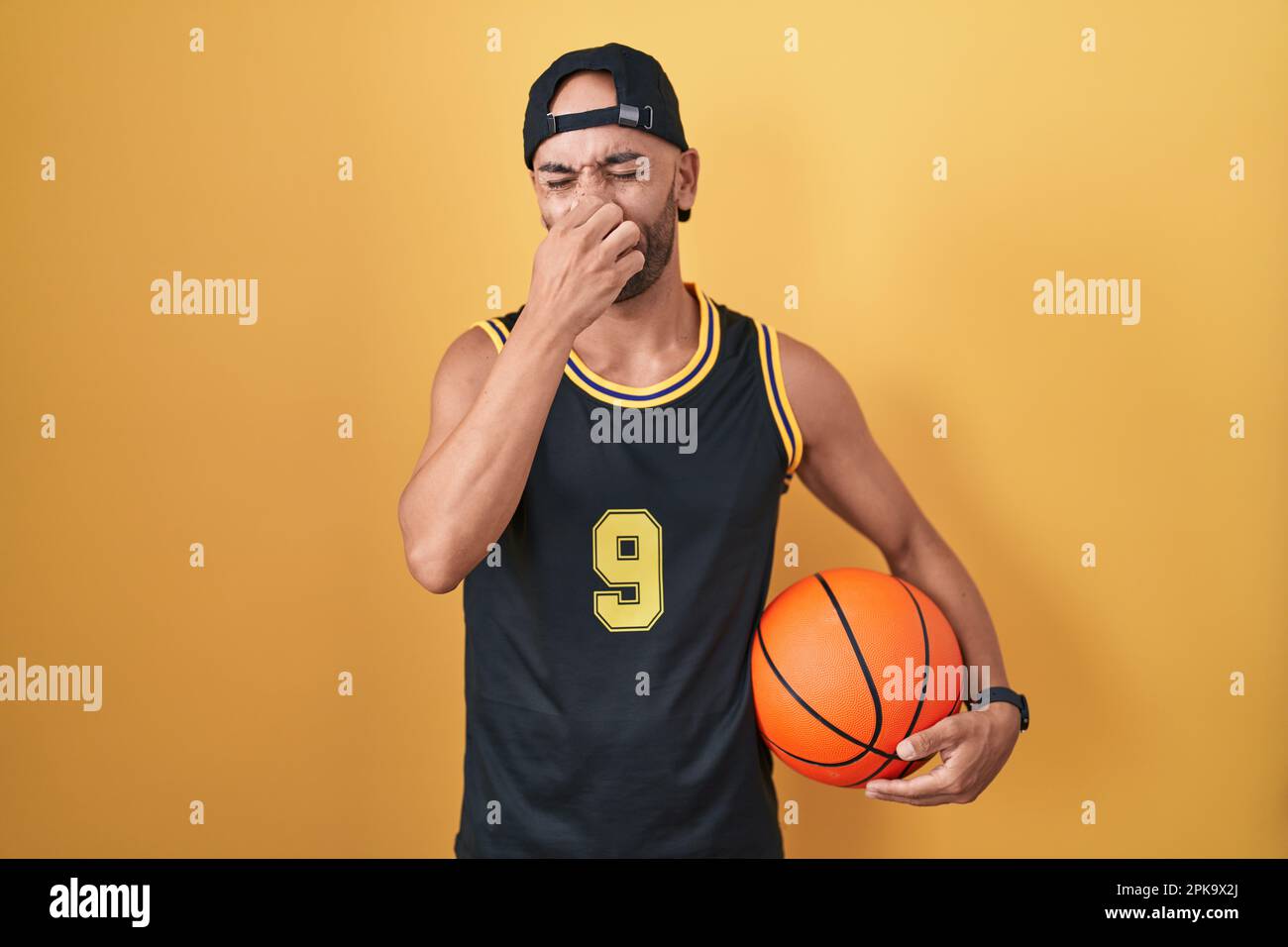 Middle age bald man holding basketball ball over yellow background
