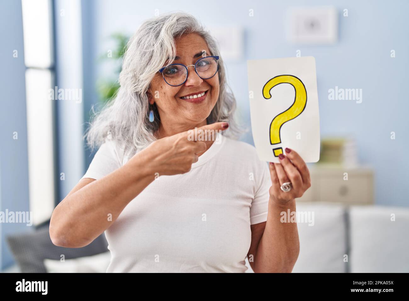 Middle age woman with grey hair holding question mark smiling happy ...