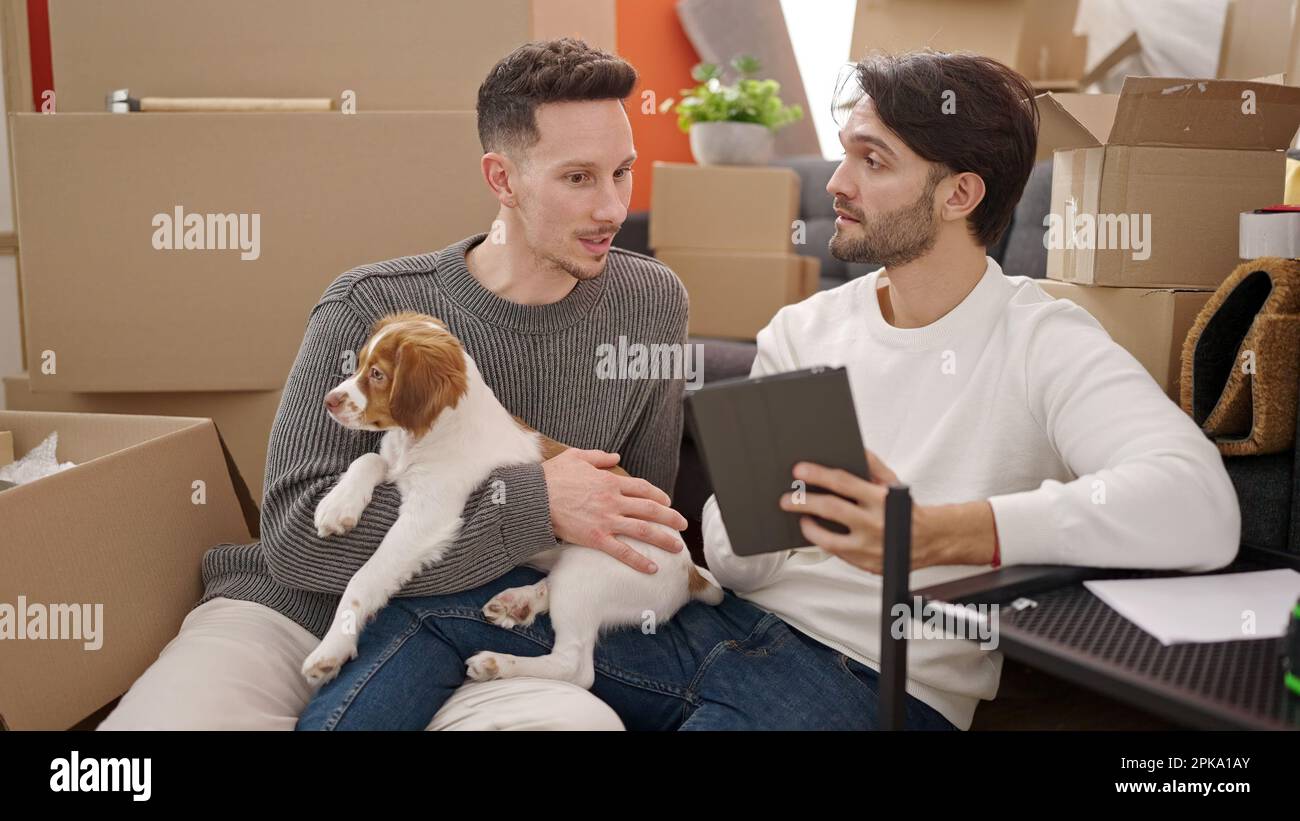 Two men couple using touchpad sitting on floor with dog at new home