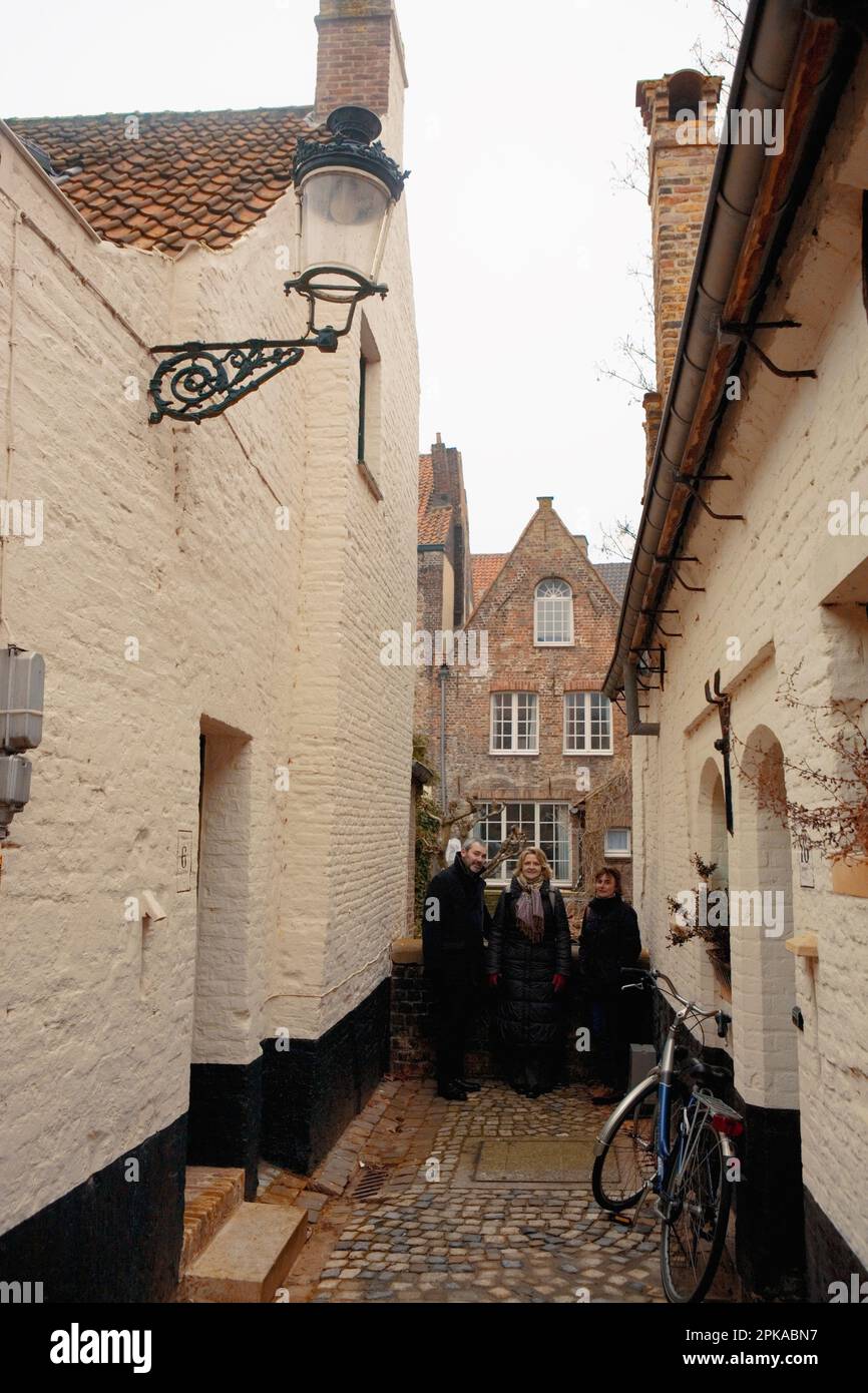 Three people stand at the end of an old alley off Moerstraat, showing former almshouse 'Vette Vispoort',1434, in Brugge, West Flanders, Belgium Stock Photo