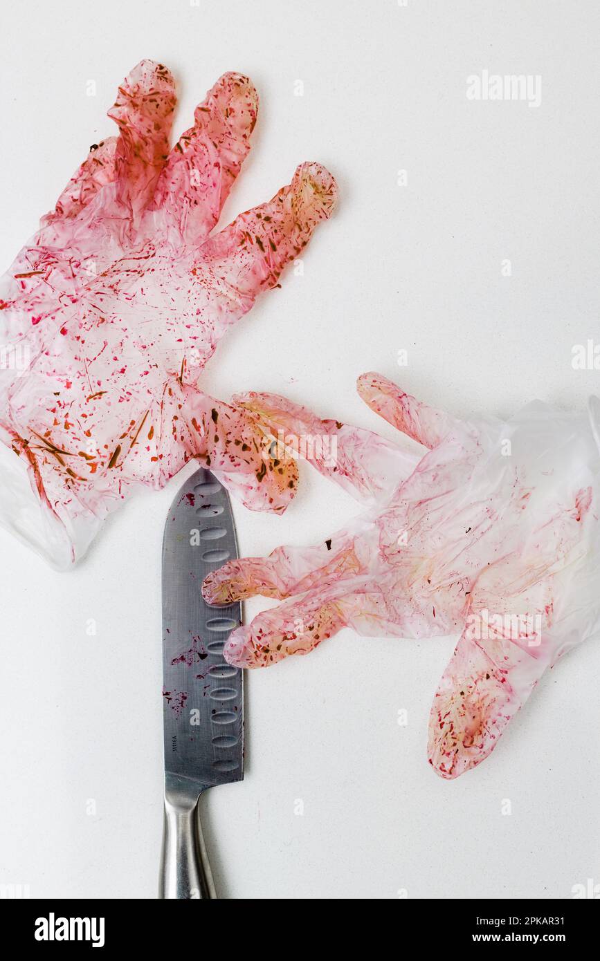 Red discolored pair of disposable glove with knife on a white surface Stock Photo