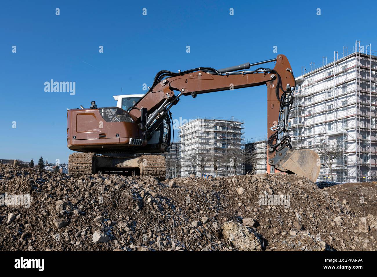 Brown excavator stands on large construction site with multistorey shell buildings in the