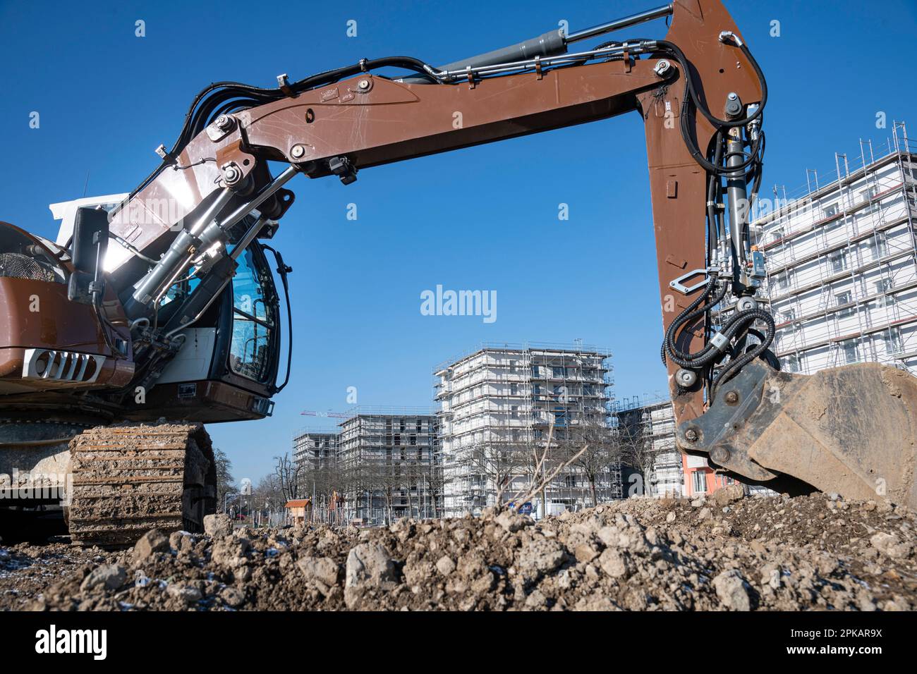 Brown excavator stands on large construction site with multistorey shell buildings in the