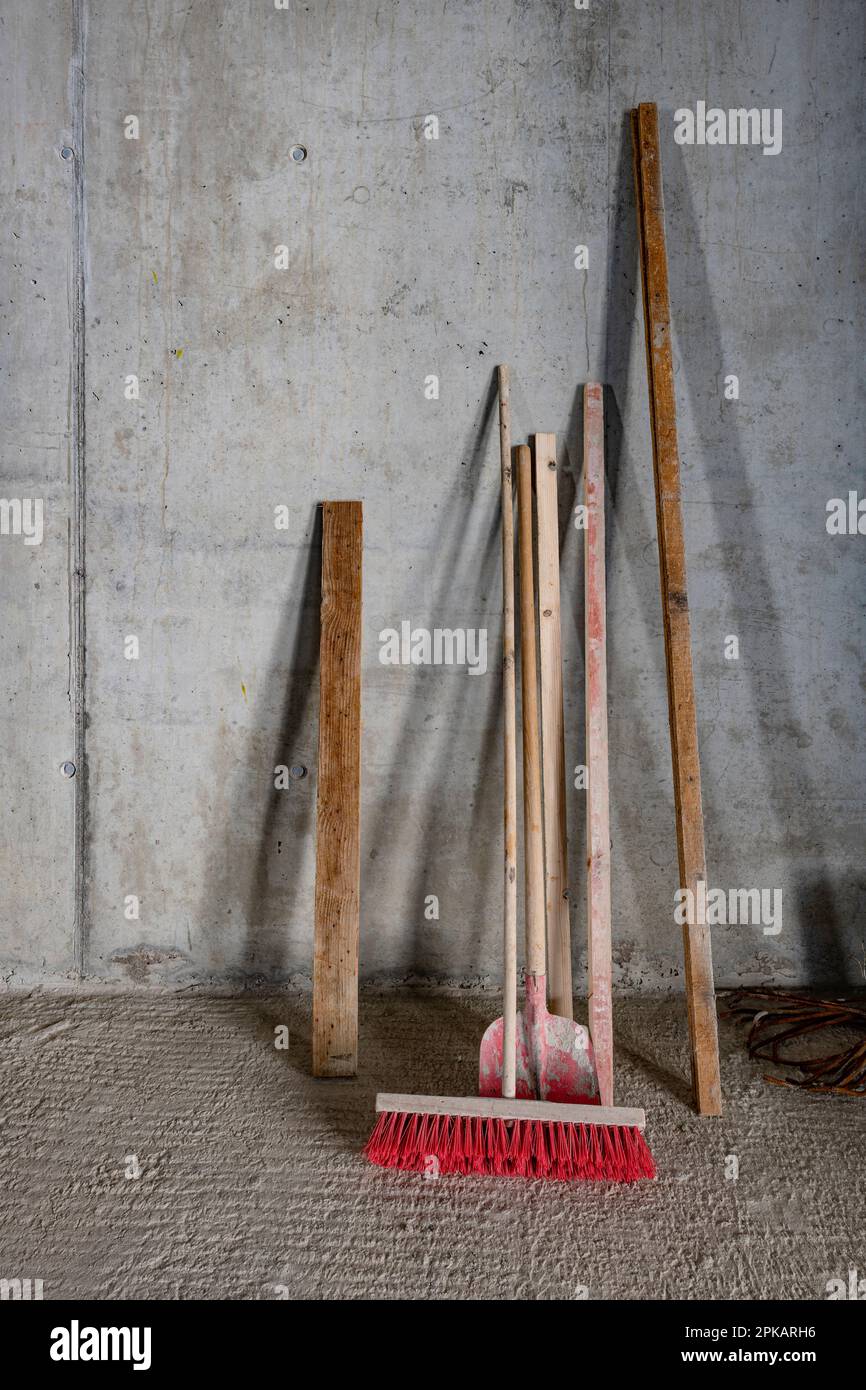 Shovel broom and wooden beam leaning against concrete wall on construction site Stock Photo