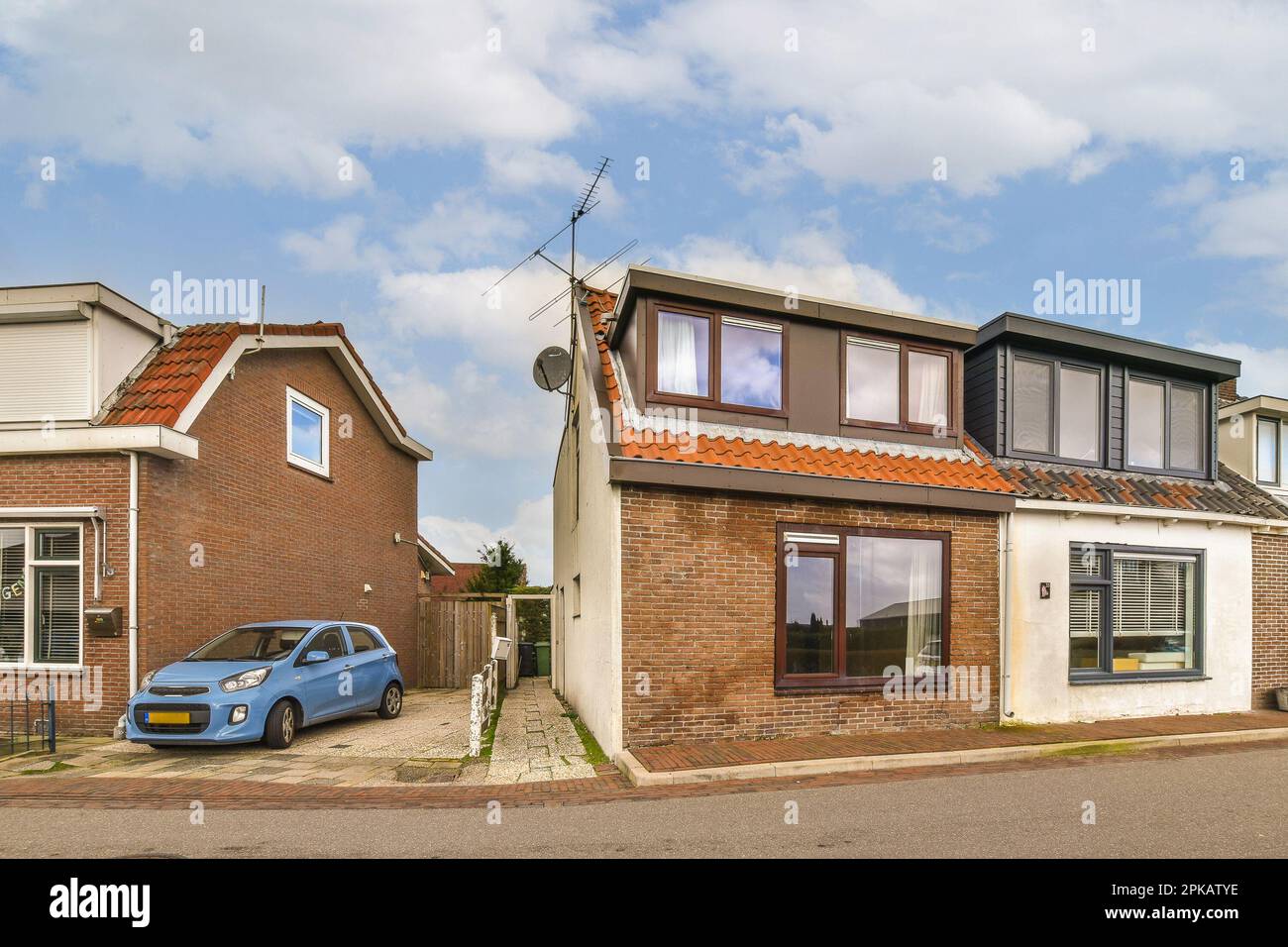 a house with a blue car parked on the street next to it and two houses