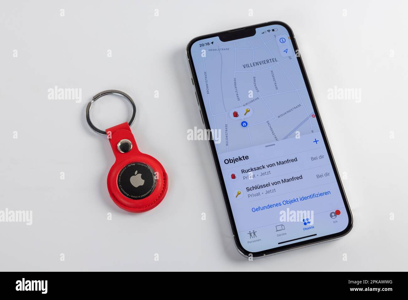 Red AirTag keychain lying next to iPhone, display, 'Where is?' App