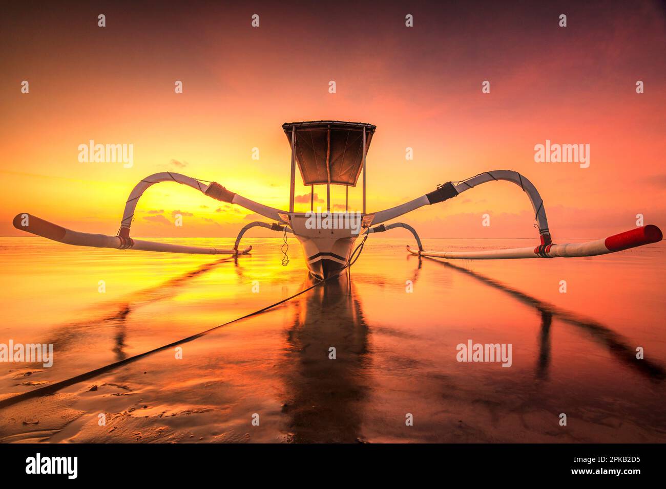 Traditional fishing boat Jukung in dreamlike sunset over the beach and sea of Sanur, Denpasar, Bali, Indonesia Stock Photo