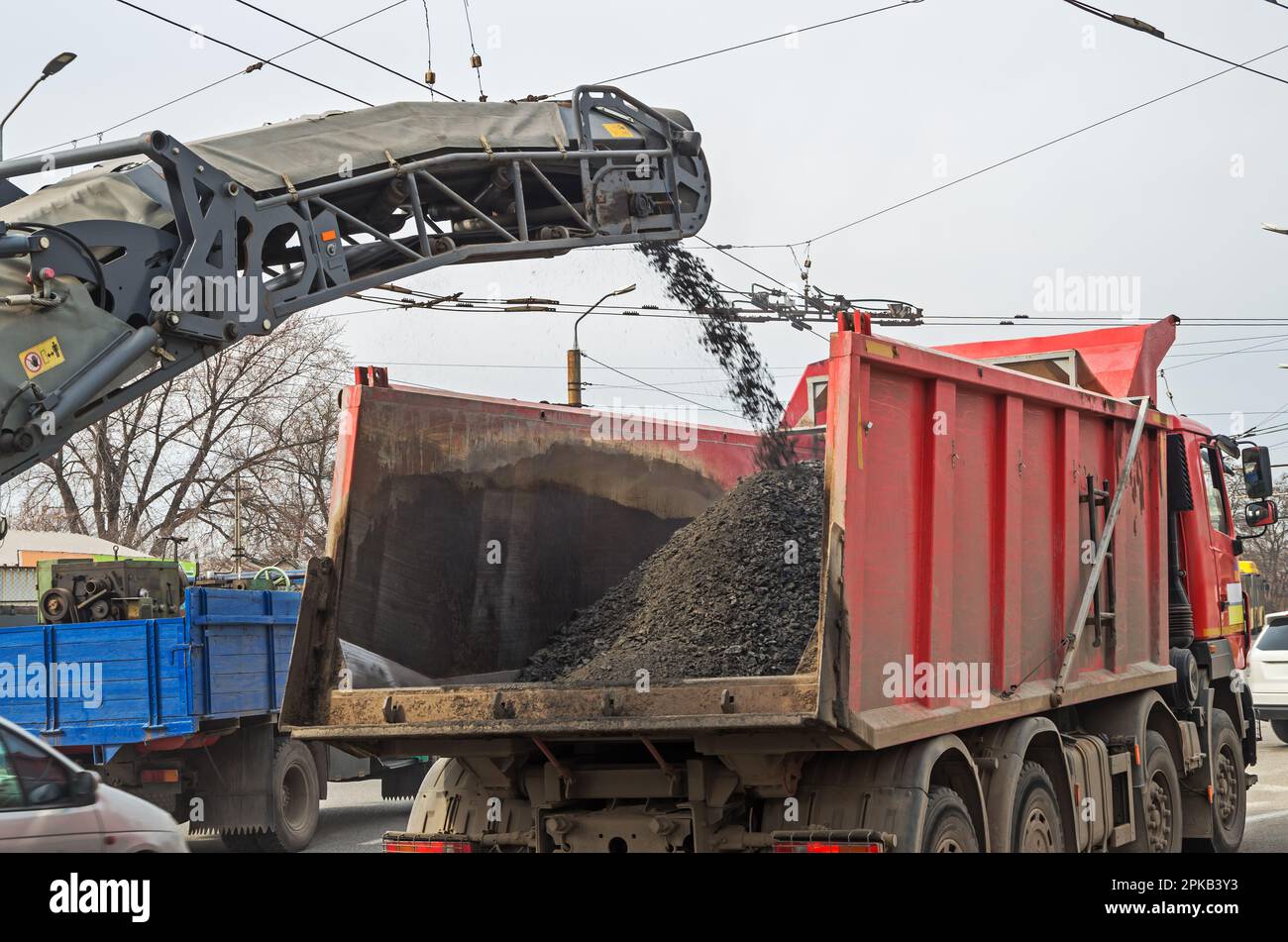 Cold planer loading crushed asphalt into dump truck on sunny spring day. Roadworks with asphalt road milling machine removing old crashed worn pavemen Stock Photo