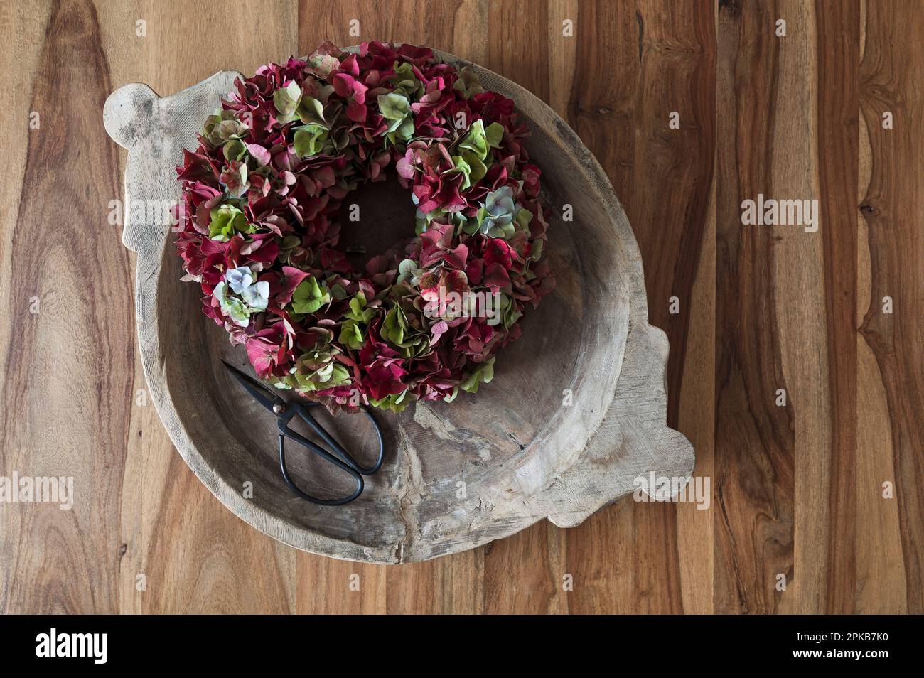 Flower wreath tied from dark red and green hydrangea flowers, arranged in old wooden bowl with flower scissors, decoration with natural materials Stock Photo