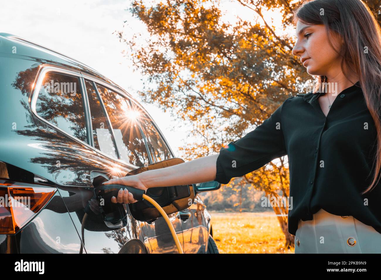 Female hand putting a cable charger in an electric car illuminated by