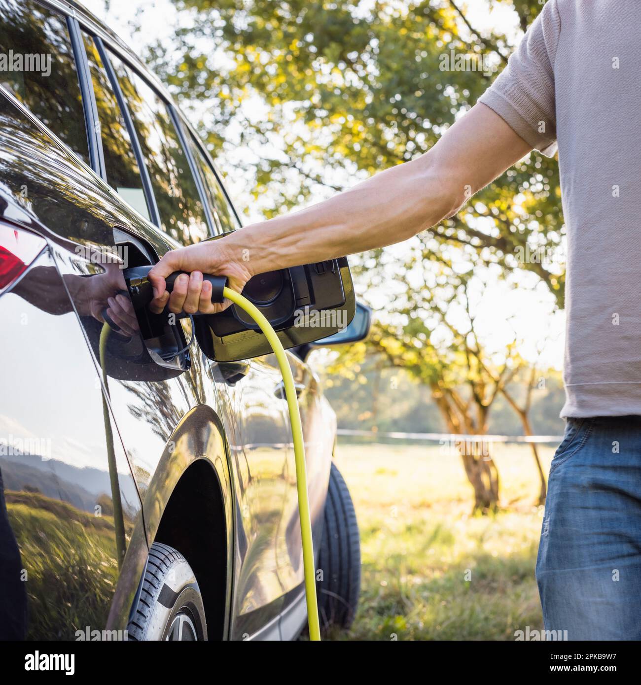 Young man plugging in the charger in a black electric car, renewable