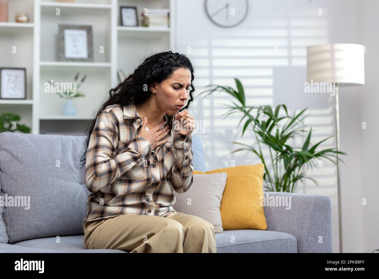 Woman having cold and sick coughing sitting on couch at home, hispanic woman in living room with cold and flu. Stock Photo