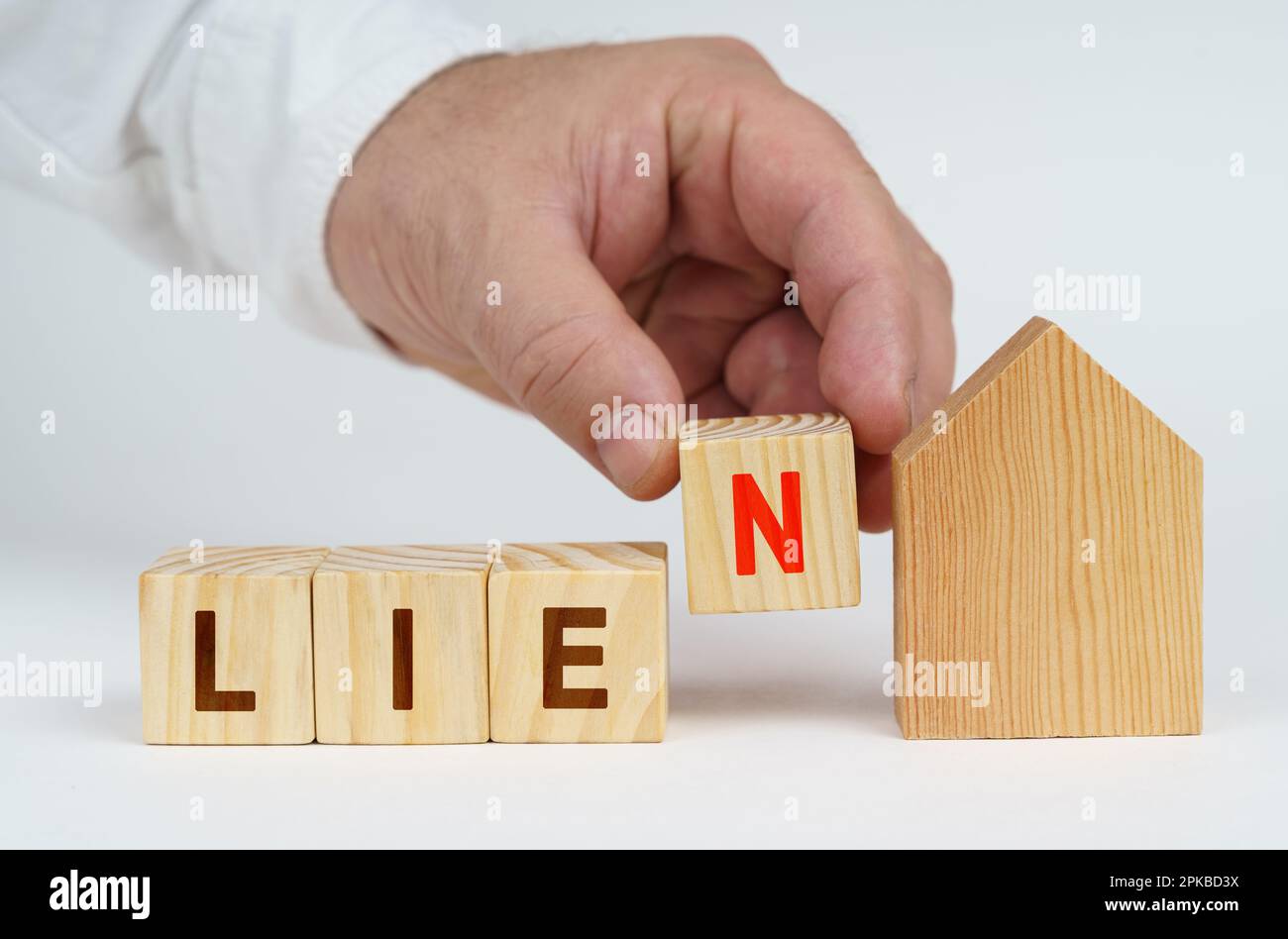 Real estate concept. On a white surface there is a model of a house, next to it a man has placed cubes with the inscription - LIEN Stock Photo