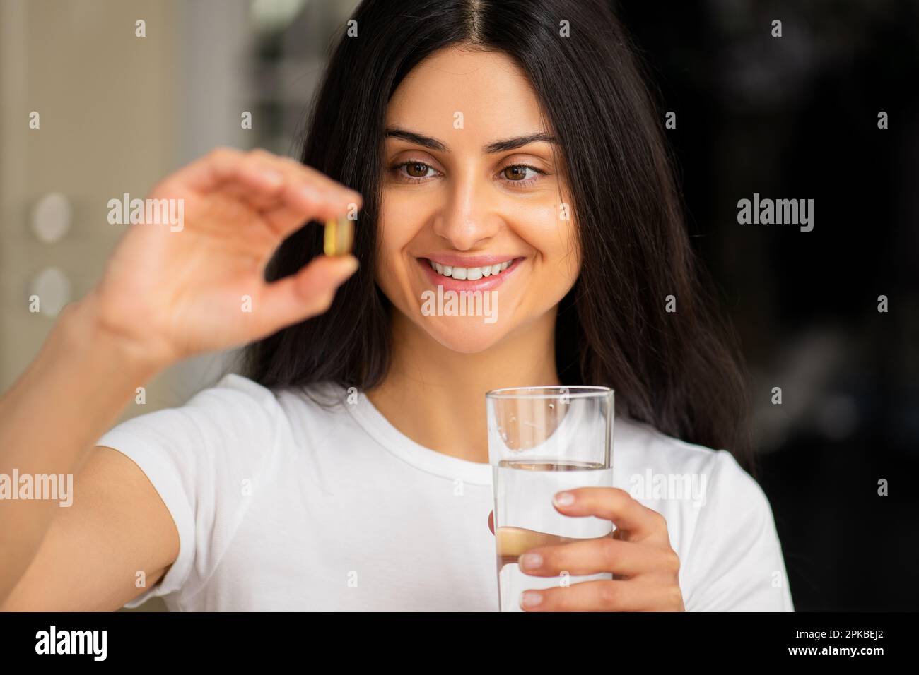 Multiracial smiling young woman taking a Fish Oil Omega3 capsule at
