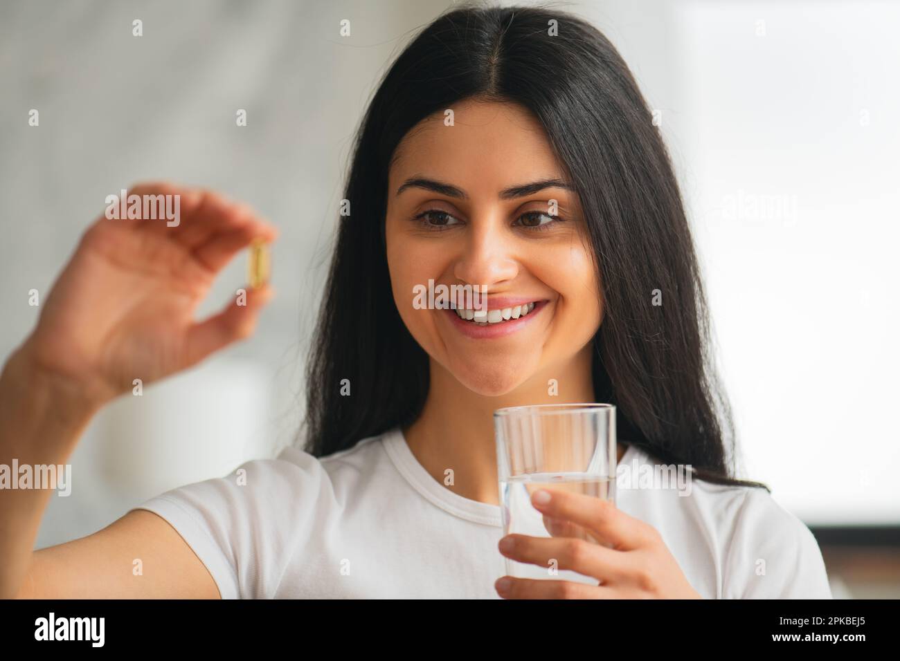 Multiracial smiling young woman taking a Fish Oil Omega-3 capsule at home with beautiful white teeth,Healthy lifestyle dietary supplements in vitamins Stock Photo