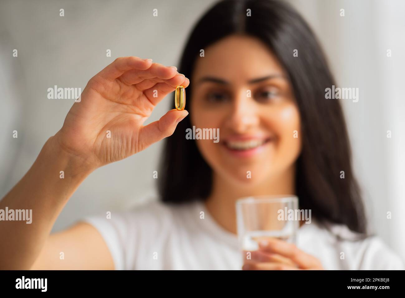Multiracial Asian smiling young woman taking a Fish Oil Omega-3 capsule at home with beautiful white teeth, Healthy lifestyle food dietary supplements Stock Photo