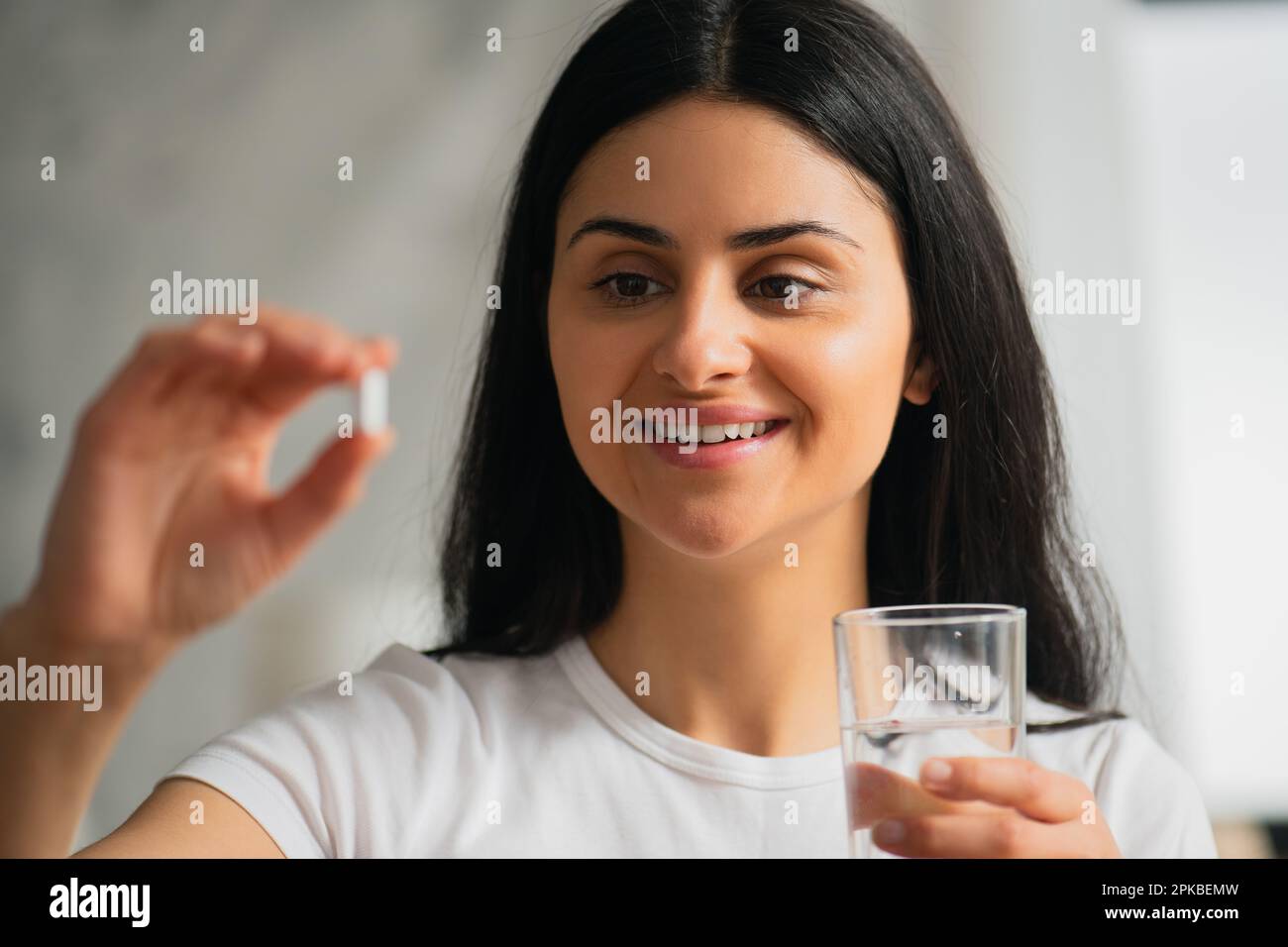 Close-up Multiracial young woman taking white capsule calcium and glass of water at home, Selective focus, Healthy lifestyle Stock Photo